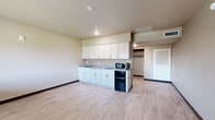 Located at 3541 E Van Buren St in Phoenix, Arizona, this single-floor unit offers a practical and well-organized layout comprising a living room, hallway, and bathroom. The open living area is finished with light wood-look luxury vinyl plank flooring and neutral-toned walls, creating a clean and versatile space. A large window along one wall allows natural light to fill the room and provides views of the surrounding neighborhood. The integrated kitchenette runs along one side of the living area and features white shaker-style upper and lower cabinets, a single-basin sink with granite-style countertop, a compact refrigerator, and a microwave — providing all the essential amenities in an efficient footprint. A hallway connects the living space to the rest of the unit and includes a closet with built-in shelving for additional storage. The bathroom is thoughtfully finished with large-format gray tile flooring, subway tile accent walls, and a walk-in shower with a white surround and chrome fixtures. Grab bars are installed for added accessibility. Throughout the unit, dark baseboards provide a clean contrast against the lighter flooring and walls, contributing to a cohesive, modern aesthetic suited to everyday living.