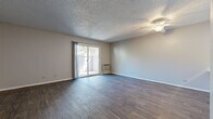 This single-floor residence in Sheridan, Colorado offers a practical and comfortable layout across three bedrooms and two bathrooms. The living room serves as the heart of the home, featuring rich, dark hardwood-style flooring, a ceiling fan, a textured ceiling, and a wall-mounted HVAC unit. A sliding glass door fills the space with natural light and opens directly onto a private, fenced patio — a secluded outdoor area surrounded by mature trees, perfect for relaxing or entertaining. The galley-style kitchen is efficiently designed with white cabinetry, light granite-look countertops, a stainless steel sink, and white appliances including a range and refrigerator, all set on easy-to-maintain wood-look flooring. The bedrooms are carpeted for comfort, with neutral tones and windows that invite natural light. The primary bedroom offers a generous footprint with its own closet featuring built-in hanging rods. Additional closet storage is also available throughout the home. The bathrooms include a tub-shower combination with a safety grab bar. Consistent textured ceilings and neutral wall tones throughout create a cohesive and move-in-ready atmosphere. A connecting hallway ties the layout together for easy navigation.