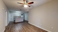 This 1-bedroom, 1-bathroom unit is thoughtfully designed with a functional open-concept layout that seamlessly connects the living area to the kitchen. The living room features rich, dark hardwood-style flooring, a ceiling fan with integrated lighting, and a front entry door flanked by windows that invite natural light into the space. Neutral gray tones on the walls create a clean, modern backdrop throughout.

The kitchen is a standout feature, equipped with granite countertops, gray cabinetry, a breakfast bar peninsula, and white appliances including an electric range, microwave, dishwasher, and refrigerator. A double-basin sink and louvered utility closet add to the kitchen's practicality.

The bedroom is generously sized, finished with plush wall-to-wall carpeting, a ceiling fan, and a window fitted with blinds that provide natural light and outdoor views. An additional carpeted room, also with a window, offers flexible use as a home office or den.

The bathroom is efficiently laid out with a granite-topped vanity, gray cabinetry, a large mirror, a tub-shower combination with tiled surround, and durable hardwood-style flooring. Every room reflects a consistent design aesthetic that balances comfort with clean, contemporary finishes.
