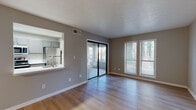 This single-floor residence at The Breck offers a thoughtfully designed layout highlighted by consistent light wood flooring and a neutral gray color palette throughout. The open living area is generously sized, benefiting from abundant natural light provided by large windows and a sliding glass door that leads to an enclosed sunroom. The sunroom, finished with whitewashed vertical wood paneling, frames serene, tree-lined outdoor views through expansive windows, creating a tranquil retreat within the unit.

The kitchen is designed in a galley configuration, featuring stainless steel appliances including a refrigerator, microwave, and range, complemented by gray cabinetry, white quartz countertops, and a classic subway tile backsplash. A pass-through window connects the kitchen directly to the living area, enhancing the sense of openness. A secondary room features a ceiling fan and access to an adjacent tiled space. Bedrooms include ample natural light and walk-in closet access. The bathroom is finished with large-format stone-look tile surrounding a soaking tub and shower combination, completing the clean, modern aesthetic found throughout the space.