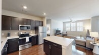 Located at 1501 Meridian Dr in Irving, TX, this well-appointed two-bedroom, two-bathroom residence offers a thoughtfully designed single-level floor plan. The open-concept kitchen and living area serves as the heart of the home, anchored by a central island with a white countertop and bar seating — ideal for casual dining or entertaining. The kitchen is outfitted with rich dark cabinetry, stainless steel appliances including a refrigerator, range, microwave, and dishwasher, complemented by gleaming hardwood-style flooring that flows throughout the main living areas. Recessed lighting adds a clean, modern feel, while large windows in the living room invite natural light and feature a ceiling fan for year-round comfort. Both bedrooms are carpeted and generously sized, each featuring a ceiling fan and dedicated closet space. The primary bedroom includes a spacious walk-in closet with built-in shelving and hanging rods. The bathrooms are finished with dark-framed vanity mirrors, dark cabinetry with white countertops, and one bathroom features a soaking tub. Neutral warm tones throughout create a cohesive, inviting ambiance suited for comfortable everyday living.