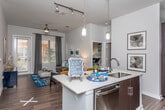 This single-floor residence offers a thoughtfully designed layout that balances modern aesthetics with everyday functionality. The open-concept kitchen serves as a central highlight, featuring dark espresso cabinetry that reaches toward the soaring ceiling, stainless steel appliances, a subway tile backsplash, and a large island with a white countertop and built-in sink — ideal for both meal preparation and casual dining. Pendant lighting adds a contemporary touch overhead.

The living area is warm and inviting, with wood-style flooring, a ceiling fan, and generous windows that draw in abundant natural light and offer views of lush greenery outside.

Each bedroom is carpeted for comfort and includes large windows dressed with blinds and draping curtains. The primary bedroom is particularly spacious, accommodating a full-sized bed with ease, and connects directly to a well-designed en-suite bathroom. Both bathrooms feature dark vanity cabinetry with white countertops, tile flooring, and direct access to walk-in closets equipped with built-in shelving and hanging rods — providing ample storage.

Throughout the residence, a neutral color palette of soft grays and whites creates a clean, cohesive ambiance that feels both modern and welcoming.