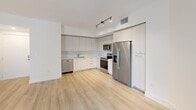This well-appointed 1-bedroom, 1-bathroom residence offers a thoughtfully designed single-floor layout with a clean, modern aesthetic throughout. Light-toned hardwood-style flooring flows seamlessly across every room, creating a cohesive and airy feel.

The kitchen is a standout feature, equipped with full-height light wood cabinetry, stainless steel appliances including a refrigerator, range, microwave, and dishwasher, complemented by a sleek white countertop and a recessed sink. Track lighting overhead adds both function and style.

The bedroom is a comfortable retreat, benefiting from two large windows fitted with horizontal blinds that frame views of lush tropical greenery, bathing the room in natural light. The space connects to a dedicated walk-in closet outfitted with multi-tiered wire shelving for organized storage.

The bathroom is finished in a neutral, spa-inspired palette featuring large-format light stone-look wall tiles surrounding a full soaking tub with shower, a floating vanity with ample under-counter storage, and light wood-tone flooring that ties the space together. Recessed lighting adds a clean, modern touch.

Overall, the residence presents a bright, minimalist aesthetic with consistent, quality finishes throughout, offering a comfortable and functional living environment.