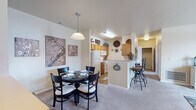 Located in Newburgh, Indiana, this single-floor residence offers a well-designed layout that balances comfort and functionality. The living room is a welcoming space, featuring plush carpeting, a large French door with transom windows that invite ample natural light and outdoor views, and generous room for seating arrangements. A pendant-lit dining area sits adjacent to the kitchen, creating a natural flow ideal for everyday meals and entertaining. The kitchen is equipped with warm wood cabinetry, a full suite of white appliances including a range with over-the-range microwave and refrigerator, a breakfast bar with seating, and durable hardwood-style flooring. The bedrooms are carpeted and comfortably sized, each offering closet storage and windows that bring in natural light. Two bathrooms serve the unit; one features a full tub-shower combination, wood vanity, and tile flooring, while the second offers a similarly appointed vanity and tile floor. Throughout the residence, neutral warm tones on the walls and soft flooring create a cohesive, inviting atmosphere that adapts easily to a variety of décor styles.