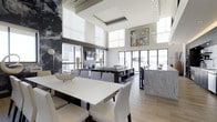 This single-floor space makes a striking impression with its soaring double-height ceilings, creating an expansive, airy atmosphere throughout. Large windows and glass doors line the perimeter, flooding the interior with abundant natural light while offering views of the surrounding exterior. A coffered ceiling detail adds architectural interest overhead, complemented by sleek pendant lighting that descends gracefully into the space.

The open-concept layout seamlessly integrates a dining area and lounge zone. The dining area features a large white rectangular table surrounded by clean-lined white upholstered chairs, anchored by light hardwood flooring. A sculptural metallic bowl serves as a refined centerpiece. Adjacent to this, the lounge area is furnished with contemporary low-profile sofas and a dark media console, creating a relaxed yet sophisticated gathering space.

A bold, large-scale artistic mural dominates one wall, adding a dramatic focal point, while a colorful framed artwork hangs on the opposite side, contributing vibrancy to the otherwise neutral palette of whites, grays, and warm wood tones. A marble-clad counter or partition is visible toward the rear, further elevating the space's upscale aesthetic. The overall ambiance is polished, modern, and welcoming.