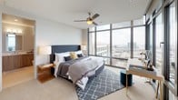 This sophisticated high-rise residence offers a seamlessly designed single-floor layout defined by clean lines, neutral tones, and an abundance of natural light. Floor-to-ceiling windows are a hallmark of the space, framing expansive urban panoramas from the living, dining, and bedroom areas alike.

The open-concept living area features built-in shelving, light hardwood flooring, and direct access to the dining room, where a striking cluster chandelier of glass pendants hangs above a solid wood dining table. A sliding glass door leads to a private balcony, extending the connection to the cityscape beyond.

The kitchen is outfitted with rich walnut cabinetry, white quartz countertops, a tiled backsplash, stainless steel appliances including a double wall oven, and a generous island that doubles as a breakfast bar — offering both functionality and style.

The bedroom is a tranquil retreat, highlighted by floor-to-ceiling windows with urban views, a ceiling fan, plush carpeting, and access to a spacious walk-in closet with dual hanging rods and shelving. Two well-appointed bathrooms serve the residence: one featuring a sleek glass-enclosed walk-in shower, the other a compact vanity with wood cabinetry and white countertop. Together, these spaces deliver a refined and comfortable urban living experience.