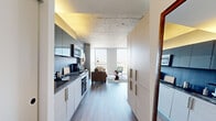 Located in Chicago's sought-after Gold Coast neighborhood, this one-bedroom, one-bathroom residence offers a thoughtfully designed layout with contemporary finishes throughout. Exposed concrete ceilings lend an industrial-chic character to the space, while light wood-tone flooring flows seamlessly from room to room.

The open-concept kitchen and living area form the heart of the residence. The kitchen is outfitted with dark stone countertops, sleek two-tone cabinetry, stainless steel appliances including a gas range and built-in microwave, and a dark tile backsplash. Tall, built-in storage cabinetry provides ample organization along the entryway corridor.

The living room is anchored by dramatic floor-to-ceiling windows that frame sweeping elevated views of the Chicago skyline and surrounding neighborhoods, filling the space with abundant natural light. A bold blue accent wall adds a pop of color and personality to the area.

The bedroom continues the concrete ceiling aesthetic and features its own large window with expansive city views, a sliding closet, and warm wood-toned furnishings. The bathroom is finished with a dark tile tub surround, a white undermount sink set in a espresso-stained vanity, and a large frameless mirror.