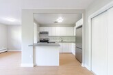 Located at 446 Kerr St in Oakville, Ontario, this one-bedroom, one-bathroom unit offers a well-designed layout with a clean, modern aesthetic. Light-toned hardwood flooring flows throughout, complementing the neutral grey walls and bright white trim that give the space a fresh, airy feel.

The open-concept living and kitchen area forms the heart of the unit. The living room is generously proportioned, with large sliding glass doors opening onto a private balcony that invites natural light and offers views of the surrounding greenery. A secondary window further brightens the space. Baseboard heating runs along the exterior walls, ensuring year-round comfort.

The kitchen is thoughtfully appointed with crisp white cabinetry extending to the ceiling, grey quartz-style countertops, a white subway tile backsplash, and stainless steel appliances including an electric range, dishwasher, and a sleek double-basin sink with a modern arc faucet. A peninsula counter provides added workspace and a natural division between the kitchen and living areas.

The bedroom is a comfortable, well-sized room with ample natural light. The bathroom features a full soaker tub with a tiled surround and grey countertop vanity. A hallway with closet storage and a dedicated entry area complete the functional layout of this well-appointed Oakville residence.