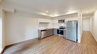 Located in Seattle's vibrant Wallingford neighborhood, this one-bedroom, one-bathroom unit offers a thoughtfully designed layout with modern finishes throughout. The open-concept kitchen and living area serves as the heart of the home, featuring wood-look flooring, recessed lighting, and a well-appointed kitchen with two-tone cabinetry, stainless steel appliances including a refrigerator, electric range, microwave, and dishwasher, plus a clean white countertop with an undermount sink. A floating wood shelf adds a warm design accent. The living area flows naturally toward a private balcony, bringing in natural light and outdoor access. The bedroom is carpeted for comfort and features a sliding barn door, adding a contemporary architectural touch, along with a separate closet for additional storage. A dedicated hallway connects the main living spaces and includes a built-in utility panel. The combined bathroom and laundry room is efficiently designed, housing a stacked Whirlpool washer and dryer unit alongside a full bathroom with wood-toned vanity cabinetry. Light, neutral tones and wood-look flooring carried throughout the unit create a cohesive, clean aesthetic that defines this modern Seattle residence.