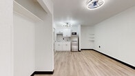Located at 3030 W Sam Houston Pkwy S in Houston, TX, this single-floor unit offers a clean, modern design with a bright and open layout. Light wood-look flooring runs continuously throughout the space, complemented by crisp white walls and bold black baseboards that create a contemporary contrast.

The open-concept living and kitchen area forms the heart of the unit. The kitchen is well-appointed with white shaker-style cabinetry, a subway tile backsplash, a stainless steel refrigerator, a built-in microwave, and a single-basin sink. A stylish sputnik-style chandelier adds a modern touch overhead, while a textured ceiling adds subtle visual interest.

The living area is open and versatile, with a wall-mounted unit for climate control and a large window fitted with roller shades that allows natural light to fill the room. The entry area features a second wall-mounted HVAC unit positioned beneath the window, along with a solid white entry door.

Built-in wall shelving in the living area provides convenient open storage. The bathroom features a wide white countertop with a vessel-style sink, a large mirror, and a shower-tub combination, maintaining the same clean aesthetic found throughout the unit. The overall ambiance is light, airy, and move-in ready.