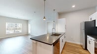 This single-floor, 2-bedroom, 1-bathroom residence offers a thoughtfully designed layout with modern finishes throughout. The open-concept kitchen and living area serves as the heart of the home, featuring a large center island with dark granite countertops, an undermount sink, and stylish pendant lighting. White shaker-style cabinetry with black hardware pairs with a subway tile backsplash and stainless steel appliances, including a refrigerator, range, microwave, and dishwasher. Light hardwood-style flooring flows through the main living areas, adding warmth and continuity. The living room benefits from large windows and a private exterior door, allowing abundant natural light and outdoor views. Both bedrooms are carpeted and feature ceiling fans, with the primary bedroom offering direct access to the full bathroom and closet. The bathroom is finished with a white vanity, dark granite countertop, and a tub-shower combination. Two walk-in closets equipped with wire shelving systems provide generous storage. Neutral tones and clean lines throughout create a bright, cohesive aesthetic well-suited for comfortable everyday living.