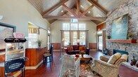 Located at 5799 Southland Dr in Mobile, Alabama, this single-floor community space showcases a compelling blend of rustic charm and welcoming design. The centerpiece of the main hall is a dramatic vaulted ceiling adorned with exposed wood trusses and tongue-and-groove wood planking, soaring overhead to create an impressive sense of openness and volume. Rich hardwood floors run throughout, complementing the warm wood wainscoting that lines the lower walls.

A floor-to-ceiling stacked stone fireplace anchors one end of the main gathering area, serving as a striking architectural focal point. Multiple seating arrangements — including leather sofas, wicker chairs, and upholstered armchairs — create inviting conversation areas beneath the cathedral ceiling. Large multi-pane windows flood the interior with abundant natural light, offering views of the surrounding landscape.

A built-in bar counter with granite surfaces and bar-height seating provides a functional area for refreshments, while an adjacent kitchenette nook offers a coffee station, mini-refrigerator, and casual dining seating with eclectic wall art. French doors with glass panels lead to additional office or multipurpose rooms, and exterior glass doors open to an outdoor area. The overall ambiance is warm, inviting, and distinctly lodge-inspired.