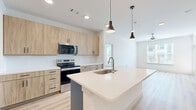 Located in Lewisville, TX, this thoughtfully designed 2-bedroom, 3-bathroom residence offers a clean, contemporary aesthetic throughout. Light-toned luxury vinyl plank flooring runs seamlessly across the entire floor, complementing the crisp white walls and creating a bright, cohesive feel.

The open-concept kitchen and living area serves as the heart of the home. The kitchen is equipped with stainless steel appliances, including a French-door refrigerator, electric range with over-the-range microwave, and a dishwasher. Light wood-grain cabinetry lines the walls floor-to-ceiling, paired with white quartz countertops and a subway tile backsplash. A central island with an undermount sink and pendant lighting above provides additional prep space and casual seating. The adjoining living area features large windows with outdoor views and a ceiling fan, filling the space with natural light.

Both bedrooms are comfortably scaled, with the primary bedroom offering direct access to an en-suite bathroom and a walk-in closet with built-in shelving. The bathrooms are finished with warm wood vanities, white quartz countertops, large-format tile surrounds in the shower areas, and wood-toned flooring. Two dedicated closets throughout the unit provide ample storage. The overall ambiance is modern, clean, and move-in ready.