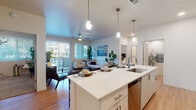 This single-floor residence is designed with a clean, contemporary aesthetic throughout. The open-concept layout connects the kitchen and living area seamlessly, creating a bright and functional shared space. The kitchen is outfitted with white shaker-style cabinetry, quartz countertops, stainless steel appliances, and a large center island with pendant lighting overhead and bar seating for casual dining. Light wood-style flooring runs throughout the main living areas, enhancing the airy feel of the space.

The living room receives generous natural light through a sliding glass door that opens to a private balcony, complemented by vertical blinds for privacy control. A ceiling fan adds comfort to the space.

The residence includes multiple bedrooms, each finished with plush carpet, ceiling fans, and natural light from windows with blinds. Both bedrooms feature walk-in closets, offering ample storage. The primary bathroom includes a dual-sink vanity with quartz countertops and white cabinetry, while the secondary bathroom features a single vanity and a tub-shower combination.

A dedicated in-unit laundry room houses a full-size washer and dryer alongside built-in shelving for added storage convenience.