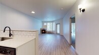 This well-appointed single-floor residence offers a clean, contemporary design with a thoughtful layout. The open living area is a standout feature, showcasing light wood-style flooring, crisp white walls, and a tile-surround fireplace positioned beneath a bank of windows that invite natural light and views of surrounding greenery. A sliding glass door provides direct access to an outdoor balcony, extending the living space outdoors. The kitchen is designed for functionality and style, featuring white shaker cabinetry, a classic subway tile backsplash, light quartz countertops, and a full suite of stainless steel appliances including a gas range, built-in microwave, dishwasher, and refrigerator. A peninsula with bar-top seating separates the kitchen from the main living area, creating an open, connected feel. The bedrooms are finished with plush carpeting and offer generous proportions, with the primary bedroom featuring its own sliding glass door leading to a private outdoor space. The bathroom is finished with light wood-look tile flooring, white cabinetry, and matte black hardware accents, contributing to the residence's modern aesthetic. Throughout the space, a neutral color palette and consistent finishes create a cohesive, inviting atmosphere.