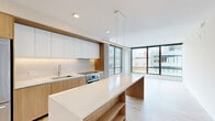Located at 42 Ridge Square in Washington, DC, this modern 2-bedroom, 2-bathroom residence offers a thoughtfully designed open-concept layout with clean lines and contemporary finishes throughout. Light hardwood flooring runs throughout the living areas and bedrooms, complementing the bright, neutral palette that defines the space.

The kitchen is a standout feature, showcasing a sleek design with a combination of white upper cabinetry and warm wood-toned lower cabinets. A generous waterfall island with built-in shelving provides ample prep space and storage. Stainless steel appliances, including a French door refrigerator and built-in oven, add a polished touch, while under-cabinet lighting enhances the modern aesthetic.

The open living area flows naturally from the kitchen and is bathed in natural light from expansive floor-to-ceiling windows with dark-framed detailing, offering views of the surrounding Washington, DC cityscape. Both bedrooms continue the bright, airy theme, each featuring large windows that frame urban vistas and dedicated closet space.

The bathrooms are finished with large-format tile flooring, wood-accented vanities topped with white countertops, and glass-enclosed showers. Two closets provide additional storage throughout the residence. The overall ambiance is clean, modern, and urban.