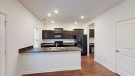 This two-story home offers a well-organized layout with distinct living spaces spread across both floors. The kitchen serves as a central highlight, featuring rich dark espresso cabinetry, dark granite-style countertops, and black appliances including a range, microwave, and refrigerator. A peninsula with a built-in sink adds prep space and a natural divide between the kitchen and adjoining areas. Hardwood-style flooring runs throughout the main level, complementing the neutral white walls and recessed lighting overhead.

A built-in desk area with matching dark cabinetry and granite-style countertops provides a dedicated workspace or study nook. The main level also includes a compact half bathroom with a pedestal sink and hardwood-style flooring, ideal for guests.

A staircase with white balusters and a wood handrail connects the floors, leading to an open upstairs hallway. The upper level bedrooms feature plush carpeting, ceiling fans, and windows that bring in natural light. Additional bedrooms are carpeted and similarly sized. A full bathroom on the upper level includes a single-sink vanity with dark cabinetry, a large mirror, and a shower-tub combination, maintaining the consistent design aesthetic found throughout the home.