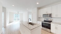 This single-floor residence at The Enzo At Ariston offers a clean, contemporary design defined by a bright, open layout and consistent use of high-quality finishes. The open-concept kitchen serves as the centerpiece of the living area, featuring a large granite-topped island with an undermount sink, white shaker-style cabinetry extending to the ceiling, and a full suite of stainless steel appliances including a refrigerator, range, and built-in microwave. Light wood-style flooring runs throughout the main living areas, complementing the crisp white walls and recessed lighting overhead.

The living area flows naturally from the kitchen and opens directly to a private balcony through sliding glass doors, allowing ample natural light to fill the space. A ceiling fan adds both function and character to this area.

The bedroom features plush carpeting, a generous window fitted with blinds, and a ceiling fan, creating a comfortable and quiet retreat. The primary bathroom is well-appointed with a double-sink granite vanity, white cabinetry, wood-style flooring, a glass-enclosed shower, and access to a walk-in closet. A secondary bathroom includes a full soaking tub and shower combination. The overall ambiance is bright, clean, and move-in ready.
