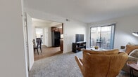 Located at 1001 Tramway Rd NE in Albuquerque, New Mexico, this one-bedroom, one-bathroom residence offers a well-organized single-level floor plan designed to maximize functionality. The living area features plush carpeting and a sliding glass door that opens to a private outdoor patio, bringing in natural light and providing a seamless indoor-outdoor connection. A secondary living area offers additional flexible space, also finished with soft carpet and neutral walls throughout. The dedicated dining area is defined by hardwood-style flooring and an overhead pendant light, creating an inviting space for meals and gatherings. The galley-style kitchen is outfitted with rich dark wood cabinetry, light countertops, black appliances including a full-size refrigerator and range, and hardwood-style flooring, with a window that allows natural light to brighten the workspace. The bedroom is a comfortable retreat featuring carpet flooring, a large window with outdoor views, and access to a dedicated closet. The bathroom includes a full shower-tub combination in a clean, white finish. A textured ceiling is consistent throughout the home, complementing the light, neutral color palette that gives the entire space a bright and cohesive feel.