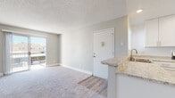 Located at 1225-1237 Graves Ave in El Cajon, California, this single-floor unit presents a clean, updated interior with a thoughtful layout designed for comfortable everyday living. The open-concept living and dining area is finished with plush carpet and neutral gray walls, creating a bright and welcoming atmosphere. A sliding glass door leads to a private balcony, allowing natural light to fill the space and offering views of the surrounding neighborhood.

The kitchen is well-appointed with white shaker-style cabinetry, stainless steel appliances including a refrigerator and electric range, and light granite-style countertops that extend to a peninsula with a sink. Wood-look flooring runs throughout the kitchen, complementing the cabinetry's clean aesthetic. A ceiling fan overhead adds to the functionality of the adjacent living space.

The bedrooms are carpeted and generously sized, with multiple windows providing ample natural light and views of the outdoors. One bedroom features a spacious walk-in closet, offering notable storage capacity. The bathroom is tastefully updated with white shaker vanity cabinets, granite-style countertops, a large mirror, wood-look flooring, and a tiled shower-tub combination with a window above for added ventilation and light.