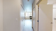 This studio in Seattle, WA is thoughtfully designed to maximize functionality within a compact footprint. The layout is organized around a single open-plan kitchen and living area, where warm wood-toned cabinetry contrasts with crisp white countertops and walls. The kitchen is fully equipped with stainless steel appliances — including a refrigerator, range, built-in microwave, and dishwasher — all illuminated by sleek track lighting overhead. Light wood-tone flooring runs throughout, lending warmth and visual continuity to the space. A large window in the kitchen and living area invites natural light and frames views of the surrounding Seattle cityscape. The entry corridor is flanked by two closets, offering generous storage for a studio of this scale. The bathroom features a warm wood vanity with a white countertop, a large mirror, and a combined shower and tub, maintaining the same consistent design palette found throughout the unit. Clean white walls and neutral finishes give the space an open, airy ambiance that feels both modern and welcoming, making it a highly efficient and practical urban living option.