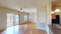 This single-floor residence offers a thoughtfully designed layout that balances open communal areas with comfortable private spaces. The living and dining areas are generously proportioned, featuring warm hardwood-style flooring, neutral beige walls, and ceiling fans with integrated lighting throughout. A sliding glass door in the living area provides direct access to an outdoor space while allowing natural light to fill the room. A standard window further brightens the space, offering views of surrounding greenery.

The kitchen is designed for functionality, featuring a galley-style configuration complemented by an open peninsula with a built-in sink and dark granite-style countertops. Rich wood cabinetry with ample storage lines the walls, and black appliances—including a range, microwave, refrigerator, and dishwasher—provide a cohesive aesthetic. Tile flooring completes the kitchen area.

The bedrooms are carpeted for comfort, each equipped with ceiling fans and windows that admit natural light. The primary bedroom includes access to a walk-in closet, adding practical storage. The bathroom features tile flooring, a wood vanity with dark countertops, overhead cabinetry, and a full bathtub. Overall, the space presents a clean, functional, and inviting atmosphere.