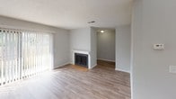 This two-story residence offers a practical and comfortable layout spread across two levels. The main living area is a welcoming, open space finished with wood-look flooring and bathed in natural light from large sliding glass doors that frame views of surrounding greenery. A classic fireplace with a white surround serves as a focal point in the living room, adding warmth and character to the space. The adjoining area flows seamlessly, connected by consistent flooring and neutral gray walls throughout.

The galley-style kitchen is efficiently designed with white cabinetry lining both sides, warm brown countertops, a stainless steel sink, and a coil-top electric range. An electrical panel is accessible just off the kitchen, and overhead ventilation ensures functionality.

The bedrooms are carpeted for comfort and feature windows fitted with blinds that allow for natural light and privacy. Multiple sliding glass doors provide additional outdoor access directly from the living spaces, opening to views of mature trees and landscaping.

The bathrooms are cleanly appointed, with one featuring a full tub-shower combination, a single-basin vanity with white cabinetry, and wood-look flooring. A separate water closet offers added convenience. Textured ceilings are consistent throughout the home, completing its straightforward and functional character.