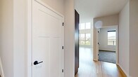 Located at 8421 Mansion Hill Ave, this two-floor residence offers a well-designed layout across a spacious main level and a comfortable upper level. The main floor is generously proportioned, anchored by an open living area with striking double-height ceilings that create an airy, expansive atmosphere. Light hardwood flooring flows throughout, complementing the clean, neutral palette of the walls. The modern kitchen features a peninsula with a built-in sink, dark cabinetry, stainless steel appliances—including a refrigerator, microwave, and range—and recessed lighting, making it both functional and stylish. A dedicated laundry area with a full-size washer and dryer provides added convenience, situated adjacent to the full bathroom, which is finished with light hardwood flooring and clean, simple fixtures. A staircase leads to the upper level, where the private bedroom offers plush carpeting, a ceiling fan, a wall-mounted mini-split HVAC unit for personalized climate control, and a window with a balcony view overlooking open green fields. A closet and hallway complete the upper floor. Throughout the home, abundant natural light, scenic outdoor views, and thoughtful finishes come together to create a bright, comfortable living environment.