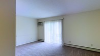 This two-floor residence offers a clean, functional layout with a calm and comfortable ambiance throughout. The main living area is finished with wall-to-wall carpeting that adds warmth underfoot, while neutral-toned walls provide a versatile backdrop suited to a variety of interior styles. A standout feature of the living space is the full-width sliding glass door, dressed with vertical blinds, which floods the room with abundant natural light and frames a verdant outdoor view of mature shrubs and greenery. This seamless connection to the outdoors enhances the sense of openness within the space. The smooth, white ceiling and clean baseboards contribute to the room's tidy, well-maintained character. Spanning two floors, the residence provides a natural separation between living and private spaces, offering both functionality and comfort. The overall atmosphere is bright, airy, and move-in ready, making it a practical and welcoming home for a wide range of occupants.