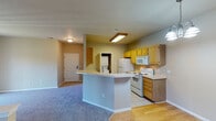 This single-floor residence offers a practical and comfortable layout with clearly defined living spaces throughout. The kitchen serves as a functional centerpiece, featuring warm honey-toned wood cabinetry lining both walls, light-colored countertops, and a full suite of white appliances including a refrigerator, electric coil range, built-in microwave, and dishwasher. Light tile flooring runs underfoot, and a dedicated in-unit laundry closet with a stacked washer and dryer adds exceptional convenience. A peninsula with a sink opens the kitchen toward the adjacent living and dining areas, creating a connected, open-concept flow.

The living area is generously sized, finished with plush blue-grey carpet and neutral beige walls that lend a calm, understated ambiance. A sliding glass door floods the space with natural light and provides access to the outdoors, while a front entry door with a sidelight panel adds architectural interest. The bedrooms continue the carpeted flooring and neutral palette, each offering ample wall space and windows that bring in natural light.

The bathroom is finished with tile flooring and includes a tub-shower combination, a vanity with wood cabinetry, and a wall mirror — practical and clean in design. Overall, the space presents a cohesive, move-in ready environment suited for a range of lifestyles.