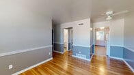 Located at 1202 E San Miguel St in Colorado Springs, Colorado, this single-floor home presents a straightforward, well-maintained layout with consistent design elements throughout. Warm hardwood flooring runs across the main living areas and bedrooms, complemented by a two-tone gray color scheme featuring lighter upper walls and deeper gray lower wainscoting with crisp white trim. The open living area is bright and cleanly finished, with ceiling-mounted HVAC vents ensuring year-round comfort. Multiple bedrooms are generously proportioned, each featuring hardwood floors, ceiling fans with light fixtures, and sliding windows that invite natural light. One bedroom offers a particularly notable view of the surrounding mountains and neighborhood greenery. The kitchen is functionally equipped with white cabinetry, dark laminate countertops, a stainless steel double-basin sink, and a freestanding electric range. The bathroom is finished with neutral stone-look tile flooring, a full tub-shower combination with white subway tile surround, and chrome fixtures. The overall ambiance of the home is clean, practical, and move-in ready, making it a solid single-floor residence in an established Colorado Springs neighborhood.