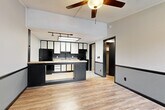 Located at 1902 Lakeshore Dr in Fort Oglethorpe, Georgia, this single-floor home offers a cohesive and functional layout with a distinctly bold design aesthetic. Throughout the space, light wood-look flooring contrasts sharply with dark trim and door frames, creating a striking two-tone visual style that carries from room to room.

The open living and kitchen area serves as the heart of the home. The kitchen is well-appointed with two-tone cabinetry — white upper cabinets paired with dark lower cabinets — a butcher block breakfast bar that doubles as a room divider, black appliances including a refrigerator and electric range, a tile backsplash, and a skylight panel above that floods the space with natural light. Track lighting and a ceiling fan with a light kit provide additional illumination throughout the living area.

A hallway off the kitchen leads to the bedroom, which features a ceiling fan, a built-in open closet, and the same wood-look flooring and two-tone wall treatment found throughout the home. The bathroom includes a vanity with a marble-patterned countertop, a large mirror with integrated lighting, and a tub/shower combination. A dedicated laundry area with washer and dryer hookups adds everyday convenience to this well-organized single-floor residence.