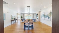 Located at 800 Aventura Way in Saint Peters, Missouri, this community clubhouse at Aventura at Richmond offers a thoughtfully designed single-floor space encompassing a diverse range of amenities. Light hardwood flooring flows throughout, unifying the open and inviting layout. The spacious living room serves as a central gathering area, anchored by a sleek tile-surround fireplace topped with a wall-mounted TV, and bordered by large sliding glass doors that frame views of the outdoor pool area, flooding the room with natural light. Adjacent dining areas provide flexible seating arrangements, including a stylishly lit dining space with a contemporary globe chandelier and dark wood table, as well as a casual coffee bar dining nook featuring a dedicated beverage station and ample natural light from large windows. The kitchen features a peninsula with bar seating, dark countertops, white subway tile backsplash, and modern pendant lighting. A dedicated office space offers a quiet workspace complete with a desk and well-stocked bookshelf. The fitness center is equipped with cardio machines, a weight bench, wall-mounted TVs, and a ceiling fan, with windows overlooking the pool. The hallway connects each area seamlessly, contributing to an overall atmosphere that is modern, functional, and welcoming.