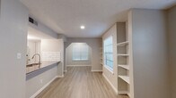 This single-floor residence offers a thoughtfully designed open layout that seamlessly connects the main living areas. Light wood-tone flooring flows throughout the living and dining spaces, complemented by neutral gray walls and crisp white trim that create a clean, contemporary aesthetic. The living room is anchored by a corner fireplace with a white mantle and features a ceiling fan with integrated lighting, along with a window that invites natural light into the space.

The kitchen is a standout area, showcasing white cabinetry, full-height white subway tile backsplash, dark stone countertops, and stainless steel appliances including a refrigerator, range, and microwave. A peninsula with an undermount sink and matching countertop provides convenient workspace and serves as a natural divider between the kitchen and the adjoining living and dining areas.

The dining area features built-in open shelving along one wall and an arched architectural detail, adding character to the space. Multiple windows fitted with blinds allow for adjustable natural light throughout.

The bathrooms are finished with neutral tones, featuring a combination tub and shower with white tile surround, brushed nickel fixtures, and a vanity with a framed mirror. A textured ceiling is present throughout the home, adding a classic touch to the overall design.