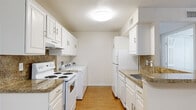 This single-floor residence offers a functional and comfortable layout designed for everyday living. The combined living and dining area is bright and welcoming, featuring neutral carpet, a ceiling fan with integrated lighting, and a decorative pendant chandelier that marks the transition into the dining space. Natural light filters in through windows, including one framing the front entry door, creating an airy feel throughout. The kitchen is designed in a galley configuration with hardwood-style flooring, white cabinetry with brushed nickel hardware, granite-look countertops, and a tile backsplash. White appliances include an electric range, refrigerator, and dishwasher. Notably, a full-size washer and dryer are also accommodated within the kitchen space, offering added convenience. A peninsula counter connects the kitchen to the dining area, providing additional prep space and a natural dividing point between the two zones. The bathroom features a tiled tub-shower combo, a toilet, and a vanity with a granite-look countertop and a large mirror. Storage is well addressed throughout the unit, highlighted by a generously sized walk-in closet with wire shelving. The hallway connects the private areas of the residence, maintaining a clear and practical flow between all spaces.