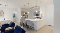 This single-story residence is designed with an open-concept floor plan that seamlessly connects the main living areas. The kitchen is a standout feature, equipped with sleek grey high-gloss cabinetry, stainless steel appliances including a French door refrigerator, built-in microwave, and range, all complemented by white quartz countertops and a white tile backsplash. A generous peninsula with seating for multiple bar stools serves as both a functional workspace and a casual dining area. Pendant lighting and a track lighting system illuminate the space effectively.

The living room offers generous proportions with high ceilings, a ceiling fan, and multiple windows that allow ample natural light. The space flows into a dedicated dining area, creating a cohesive, airy atmosphere throughout.

The primary bedroom is well-proportioned and includes natural light from a side window, while the primary bathroom impresses with a marble-surround walk-in glass shower, a separate soaking tub, a dual-sink vanity with quartz countertops, and a walk-in closet. A secondary bedroom offers comfortable dimensions and natural light. The secondary bathroom features a marble-surround tub-shower combination with clean, neutral finishes. Light wood-tone flooring flows consistently throughout the residence.