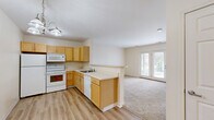 Located at 18 Pavement Rd in Lancaster, NY, this single-floor, one-bedroom, one-bathroom residence offers a well-organized and functional layout. The open-concept kitchen and living area serves as the heart of the home, with the kitchen featuring light wood cabinetry, white appliances including a refrigerator, electric range, microwave, and dishwasher, and a peninsula with a sink that provides a natural division between the kitchen and living space. The kitchen is finished with durable hardwood-style flooring, while the living area transitions to plush wall-to-wall carpeting. A chandelier overhead adds a touch of warmth to the kitchen, and a set of double French doors at the far end of the living room fills the space with natural light and provides outdoor access. The bedroom is a comfortable, carpeted room with a window offering natural light and views of surrounding greenery, supported by three closets throughout the unit for ample storage. The bathroom is finished with hardwood-style flooring and includes a single-sink vanity with warm wood cabinetry, a large mirror with overhead lighting, and a full bathtub with a curved shower curtain rod. Neutral tones and clean finishes throughout lend the space a bright, move-in-ready feel.