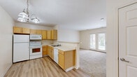 Located at 18 Pavement Rd in Lancaster, NY, this single-floor, one-bedroom, one-bathroom residence offers a well-organized and functional layout. The open-concept kitchen and living area serves as the heart of the home, with the kitchen featuring light wood cabinetry, white appliances including a refrigerator, electric range, microwave, and dishwasher, and a peninsula with a sink that provides a natural division between the kitchen and living space. The kitchen is finished with durable hardwood-style flooring, while the living area transitions to plush wall-to-wall carpeting. A chandelier overhead adds a touch of warmth to the kitchen, and a set of double French doors at the far end of the living room fills the space with natural light and provides outdoor access. The bedroom is a comfortable, carpeted room with a window offering natural light and views of surrounding greenery, supported by three closets throughout the unit for ample storage. The bathroom is finished with hardwood-style flooring and includes a single-sink vanity with warm wood cabinetry, a large mirror with overhead lighting, and a full bathtub with a curved shower curtain rod. Neutral tones and clean finishes throughout lend the space a bright, move-in-ready feel.
