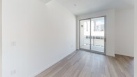 Located along the iconic Wilshire Boulevard in Los Angeles, this modern single-floor unit offers a thoughtfully designed layout with contemporary finishes throughout. Light wood-tone flooring flows seamlessly across the living areas, creating a warm yet clean aesthetic that complements the crisp white walls.

The galley-style kitchen is well-appointed with white cabinetry featuring brushed hardware, dark countertops, a stainless steel double-basin sink, and a full suite of stainless steel appliances including a refrigerator, range, microwave, and dishwasher. The kitchen opens toward the main living area, allowing natural light from the sliding glass door to filter through the space.

The living area is bright and open, anchored by a full-height sliding glass door that leads to a private balcony, offering views of the surrounding Los Angeles urban landscape. The minimalist design keeps the focus on clean lines and functionality.

The bathroom maintains the same modern aesthetic, featuring wood-look tile flooring, a walk-in shower with white subway tile surround and a linear drain, and accessibility-friendly grab bars. Recessed lighting provides a clean, well-lit environment.

Overall, this unit presents a polished, move-in-ready space ideal for urban living in the heart of Los Angeles.