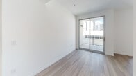 Located along the iconic Wilshire Boulevard in Los Angeles, this modern single-floor unit offers a thoughtfully designed layout with contemporary finishes throughout. Light wood-tone flooring flows seamlessly across the living areas, creating a warm yet clean aesthetic that complements the crisp white walls.

The galley-style kitchen is well-appointed with white cabinetry featuring brushed hardware, dark countertops, a stainless steel double-basin sink, and a full suite of stainless steel appliances including a refrigerator, range, microwave, and dishwasher. The kitchen opens toward the main living area, allowing natural light from the sliding glass door to filter through the space.

The living area is bright and open, anchored by a full-height sliding glass door that leads to a private balcony, offering views of the surrounding Los Angeles urban landscape. The minimalist design keeps the focus on clean lines and functionality.

The bathroom maintains the same modern aesthetic, featuring wood-look tile flooring, a walk-in shower with white subway tile surround and a linear drain, and accessibility-friendly grab bars. Recessed lighting provides a clean, well-lit environment.

Overall, this unit presents a polished, move-in-ready space ideal for urban living in the heart of Los Angeles.