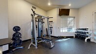 Located at 3411 N 16th St in Phoenix, Arizona, this single-story fitness center offers a well-equipped workout facility designed to support a full range of exercise routines. The space is organized into distinct functional zones, each catering to different training needs.

The cardio area features multiple treadmills, elliptical trainers, and a stair climber, all positioned along a bank of windows fitted with horizontal blinds that allow natural light to filter in. Wall-mounted flat-screen televisions are positioned throughout the space to keep users entertained during workouts.

The strength training area is anchored by a multi-functional cable and Smith machine system, accompanied by adjustable benches suitable for a variety of exercises. A dedicated free weight section includes a neatly organized dumbbell rack offering a range of weights, ideal for both beginner and advanced lifters. Additional resistance training equipment, including resistance bands and a weight plate station, rounds out the strength offerings.

The flooring throughout is durable rubber, providing traction and impact absorption across all workout zones. The interior features clean white walls, recessed lighting, and adequate ventilation. An accessible restroom and clearly marked exits contribute to a safe and inclusive environment. The open layout allows for comfortable movement between equipment, making this fitness center a practical and functional amenity.