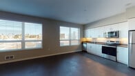 Located at 2424 Broadway in Oakland, CA, this modern single-floor unit offers a well-designed layout that balances open living space with functional rooms. The main living and kitchen area is bright and welcoming, featuring dark hardwood-style flooring throughout and multiple windows fitted with horizontal blinds that allow abundant natural light while offering views of the surrounding urban landscape.

The kitchen is thoughtfully equipped with white cabinetry, dark countertops, and a full suite of stainless steel appliances, including a refrigerator, electric range, built-in microwave, and dishwasher. Under-cabinet lighting adds a clean, modern touch to the workspace.

A hallway connects the living area to the private rooms, which include well-proportioned bedrooms with windows that bring in natural light. The primary bedroom area features a closet and is adjacent to an in-unit stacked washer and dryer, offering everyday convenience.

Two full bathrooms serve the unit, each finished with neutral tones, wood-style flooring, white tub-shower combinations, and vanities with dark countertops. The overall aesthetic throughout the unit is clean and contemporary, with a neutral color palette of warm gray and white that creates a cohesive, modern ambiance throughout this Oakland residence.