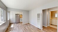 Located at 316–324 Lincoln St in Santa Cruz, California, this efficiently designed one-bedroom, one-bathroom unit offers a clean, modern aesthetic throughout its single floor. Light wood-look flooring runs continuously across the living room, bedroom, hallway, and closet, lending the space a cohesive and airy feel.

The living room greets you at the front entry, featuring a classic six-panel white front door and large windows that invite generous natural light and views of the surrounding neighborhood. A wall-mounted heater provides functional climate control without disrupting the open layout.

The kitchen is well-equipped with white shaker-style cabinetry extending to the ceiling for maximum storage, light countertops, a stainless steel refrigerator, a white range, and a brushed gold faucet over an undermount sink — a clean, functional workspace with contemporary detailing.

The bedroom is a comfortable, naturally lit retreat with a window overlooking the outdoors and a sliding-door closet, offering practical storage. The hallway connects the spaces efficiently, maintaining an organized flow throughout.

The bathroom features light tile flooring, a white vanity with an undermount sink and mirror, and a glass-enclosed walk-in shower with tile surround — a tidy, well-finished space. Overall, the unit presents a bright, neutral palette ideal for easy personalization.