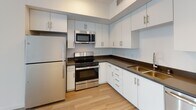 Located on Wilshire Boulevard in the heart of Los Angeles, this modern single-floor unit offers a clean, contemporary design defined by crisp white walls, light wood-tone flooring, and an abundance of natural light throughout. The open-concept layout creates a seamless flow between the living area and kitchen, where white flat-panel cabinetry, dark countertops, and a full suite of stainless steel appliances — including a gas range, microwave, and refrigerator — come together for a functional and stylish cooking space. A stacked washer and dryer are conveniently integrated into the unit. The bedroom features a reach-in closet and is bathed in natural light, with sliding glass doors providing direct access to a private balcony with railing — ideal for taking in the surrounding urban landscape. The unit includes two bathrooms: one with a tiled walk-in shower finished in glossy white tile, and another with a soaking tub and matching white tile surround with a brushed nickel fixture. Both bathrooms feature warm wood-tone flooring that complements the rest of the unit. The overall ambiance is clean, bright, and move-in ready, reflecting a modern residential aesthetic well-suited for urban living in Los Angeles.
