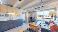 This single-floor unit showcases a thoughtfully designed industrial-contemporary interior. The open-plan living and kitchen area serves as the heart of the space, where exposed ceiling beams, visible ductwork, and a textured ceiling combine with modern finishes to create an urban loft aesthetic. Concrete flooring anchors the living area, which benefits from generous natural light through large sliding glass doors that offer views of the surrounding exterior.

The kitchen is well-appointed with two-tone cabinetry—light upper cabinets paired with dark lower units—stainless steel appliances including a full-size refrigerator, a double sink, and ample counter space. A sliding barn door separates the living zone from a dedicated dining nook.

The bedroom is a comfortable retreat featuring carpeted flooring, exposed beams, concrete block walls painted in soft tones, and its own large sliding glass door that fills the room with natural light. A spacious walk-in closet with built-in shelving and wall hooks provides practical storage.

The bathroom is clean and functional, finished with wood-toned cabinetry, a single vanity with an integrated sink, and a full shower-tub combination. The overall ambiance throughout is modern, efficient, and urban in character.