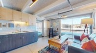 This single-floor unit showcases a thoughtfully designed industrial-contemporary interior. The open-plan living and kitchen area serves as the heart of the space, where exposed ceiling beams, visible ductwork, and a textured ceiling combine with modern finishes to create an urban loft aesthetic. Concrete flooring anchors the living area, which benefits from generous natural light through large sliding glass doors that offer views of the surrounding exterior.

The kitchen is well-appointed with two-tone cabinetry—light upper cabinets paired with dark lower units—stainless steel appliances including a full-size refrigerator, a double sink, and ample counter space. A sliding barn door separates the living zone from a dedicated dining nook.

The bedroom is a comfortable retreat featuring carpeted flooring, exposed beams, concrete block walls painted in soft tones, and its own large sliding glass door that fills the room with natural light. A spacious walk-in closet with built-in shelving and wall hooks provides practical storage.

The bathroom is clean and functional, finished with wood-toned cabinetry, a single vanity with an integrated sink, and a full shower-tub combination. The overall ambiance throughout is modern, efficient, and urban in character.