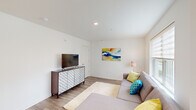 This three-floor home provides a well-organized layout across its multiple levels, offering generous living space distributed thoughtfully between floors. The ground floor serves as an entry level, while the main and upper floors contain the home's primary living and sleeping areas.

The heart of the home is the open-concept main floor, where the kitchen, dining room, and living room flow seamlessly together. The kitchen features two-tone shaker cabinetry in white and soft sage green, stainless steel appliances, quartz countertops, and a large island with an integrated sink and seating for multiple guests, illuminated by a sleek oval pendant light. A sliding glass door connects the kitchen to an outdoor area, filling the space with natural light. The adjoining living area features light hardwood-style flooring, recessed lighting, and large windows.

The upper floor houses the five bedrooms, including a primary bedroom with a dedicated walk-in closet. Secondary bedrooms feature carpet flooring, generous windows for natural light, and closet storage. The three bathrooms are finished in a clean, modern style with white cabinetry featuring gold hardware, quartz vanities, illuminated mirrors, and shower-tub combinations with wood-look tile flooring, creating a cohesive and polished aesthetic throughout.