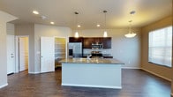 This two-story home offers a well-designed layout that balances functionality and modern style across both levels. The main floor showcases an open-concept kitchen that serves as the heart of the home. A generously sized center island with granite countertops and an integrated sink provides ample workspace and serves as a natural gathering point. Pendant lighting hangs above the island, complementing the recessed lighting throughout the space and creating a warm, inviting ambiance. Rich, dark cabinetry lines the kitchen walls, offering abundant storage, while stainless steel appliances — including a French door refrigerator with ice and water dispenser, a built-in microwave, and a range — add a sleek, contemporary touch. A dedicated walk-in pantry, visible just off the kitchen, provides additional storage and organizational space. The kitchen flows seamlessly into the adjacent living areas, enhanced by durable hardwood-style flooring that extends throughout the main level. The neutral wall tones and thoughtful lighting contribute to an open, airy feel. With its practical design, quality finishes, and cohesive aesthetic, this home offers comfortable and stylish everyday living across its two floors.