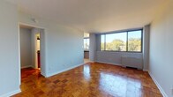 This thoughtfully designed single-floor unit offers a welcoming and functional layout throughout. The main living area is immediately striking, characterized by its beautiful herringbone-patterned parquet wood flooring that extends throughout the space, gleaming under abundant natural light. Large picture windows dominate the exterior wall of the living room, framing picturesque views of mature, lush treetops and surrounding rooftops, creating a serene, park-like ambiance from within. A radiator positioned beneath the windows completes the classic feel of this sun-filled space.

The bedroom is generously sized, continuing the warm parquet flooring, with smooth, light-toned walls and clean white trim that lend a calm and neutral palette ideal for personalization.

The kitchen is efficiently laid out and features rich, deep cherry-toned cabinetry paired with dark granite countertops, a stainless steel sink, a black gas range, and light tile flooring — a practical and stylish space for everyday cooking.

The bathroom carries the same refined aesthetic, showcasing a cherry wood vanity with a dark granite countertop and a framed mirror. Adjacent to the bathroom is a well-organized walk-in closet with built-in shelving, offering ample storage. Overall, the unit presents a cohesive blend of classic character and modern finishes.