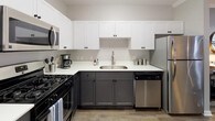This single-floor, 2-bedroom, 2-bathroom residence combines modern design with functional living across a generously sized floor plan. The living room features crown molding, wood-look flooring, and a sliding glass door that invites natural light and provides access to an outdoor area. The adjacent dining space is accented with decorative wall art and crown molding, creating a refined yet relaxed atmosphere.

The kitchen is a standout, featuring a two-tone cabinet design with crisp white uppers and charcoal lower cabinets, white countertops, and stainless steel appliances including a gas range, built-in microwave, and dishwasher — ideal for everyday cooking and entertaining.

The primary bedroom offers a calming retreat with a bold charcoal accent wall, plush carpeting, a ceiling fan, and pendant sconce lighting flanking the bed. A spacious walk-in closet with wire shelving and hanging rods provides ample storage. The primary bathroom includes a vanity with matching two-tone cabinetry, a soaking tub, a separate shower with glass enclosure, and wood-look flooring.

The second bedroom is bright and comfortable with soft gray walls, plush carpet, and dedicated closet access. Throughout, the design maintains a cohesive contemporary aesthetic with neutral tones and thoughtful detailing.